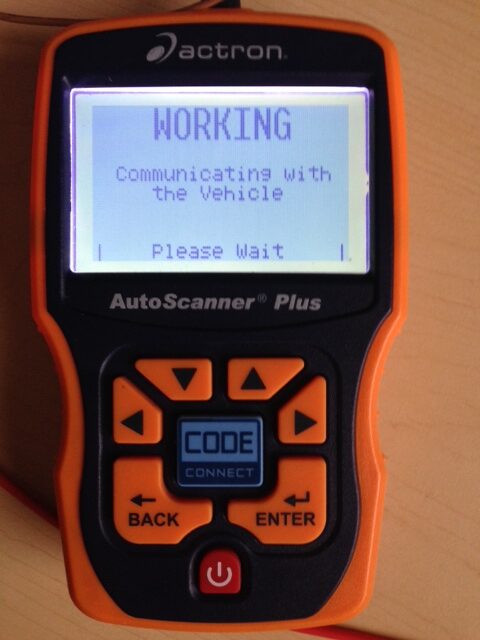 "Handheld Actron AutoScanner Plus OBD-II device with screen showing 'Working — Communicating with the Vehicle'"